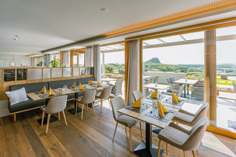 Mit gelben Servietten gedeckte Tische in einem Restaurant, Ausblick auf einen massiven Felsen mit Burg