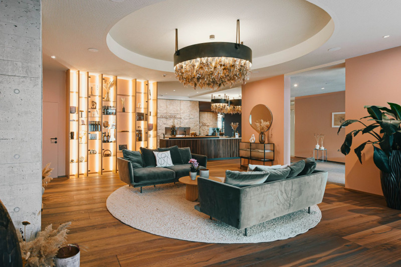 Hotellobby mit dunklegrüner Couch und Couchtisch, im Hintergrund die Rezeption